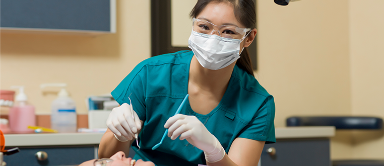 Image of a dental professional in full dental personal protective equipment tending to her patient in her dental practice