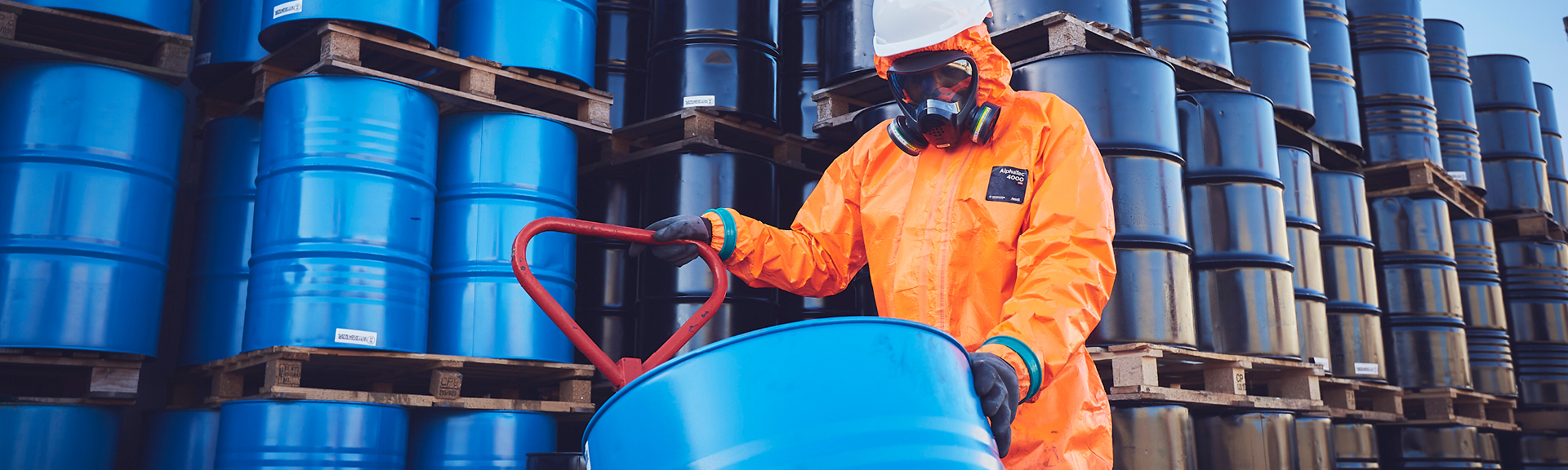 Industrial worker wearing AlphaTec protective clothing and chemical gloves while handling hazardous chemicals in manufacturing environment