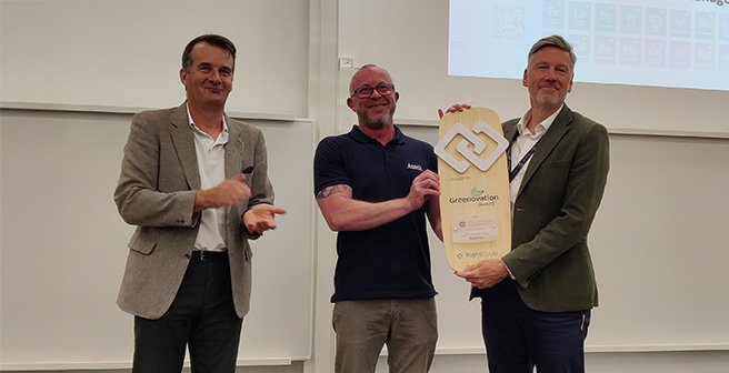 Three men standing in a lecture room during an award ceremony and holding a large wooden award plaque.