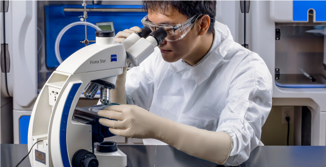 Pharmaceutical lab technician wearing long cuff examination gloves while looking through microscope