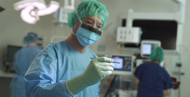 Image of a surgeon in the foreground in full PPE right before performing a surgical procedure