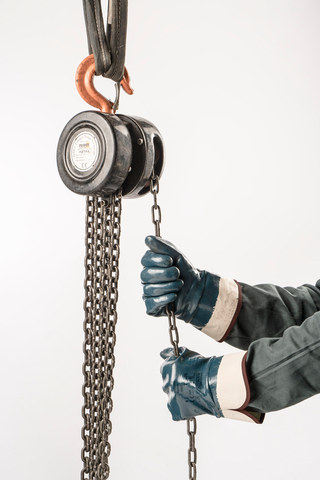 Worker wearing ActivArmr® Hycron® 27-805 protective mechanical gloves operates a heavy-duty chain hoist, pulling the chain to lift or lower a load