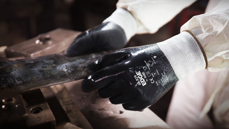 Worker wearing EDGE® 48-929 mechanical gloves engages in metallurgy tasks, handling metal materials with precision and safety.