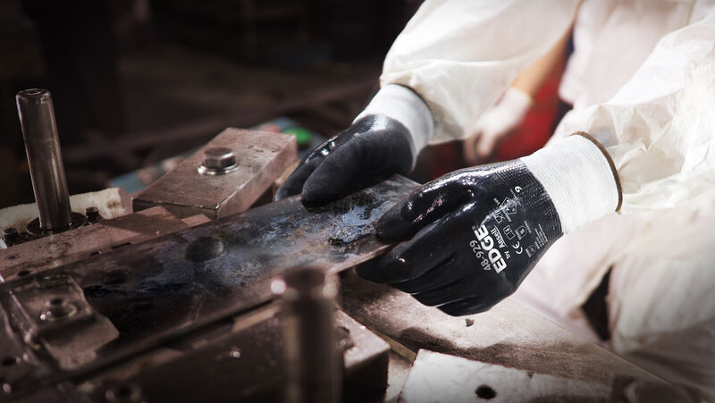 Worker wearing EDGE® 48-929 mechanical gloves engages in metallurgy tasks, handling metal materials with precision and safety.