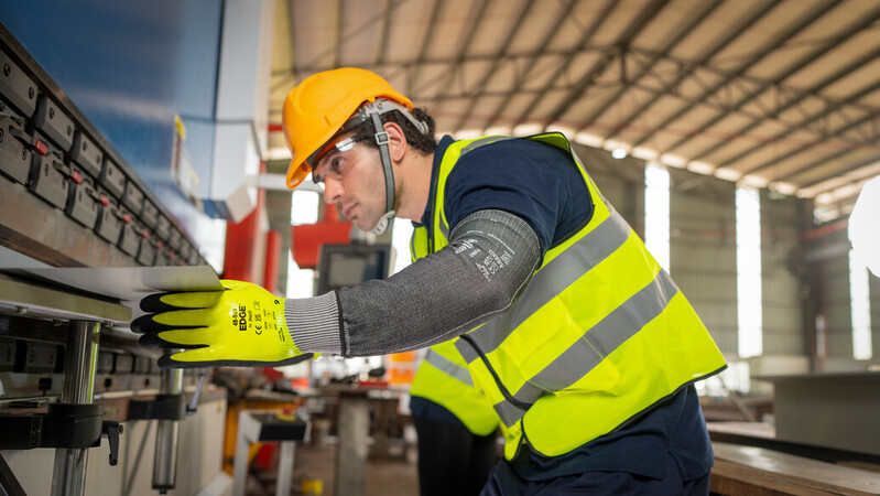 Worker wearing EDGE 48-969 mechanical gloves handles metal sheets with precision and care