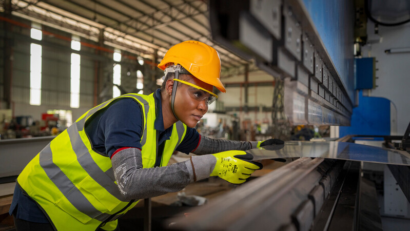 Worker wearing EDGE 48-969 mechanical gloves handles metal sheets with precision and care