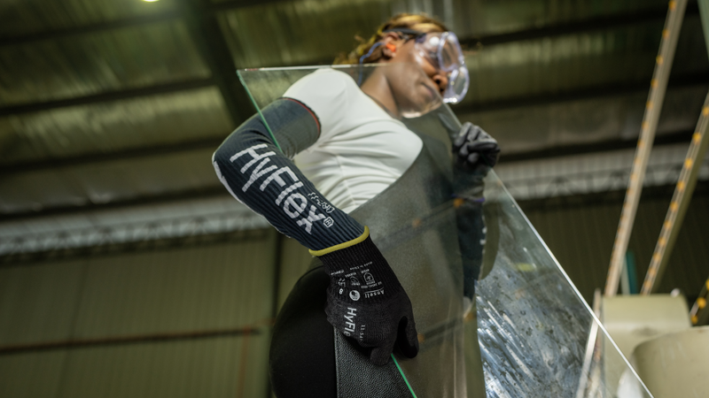 Worker carefully handles a large glass sheet in a manufacturing facility wearing HyFlex® 11-543 mechanical gloves