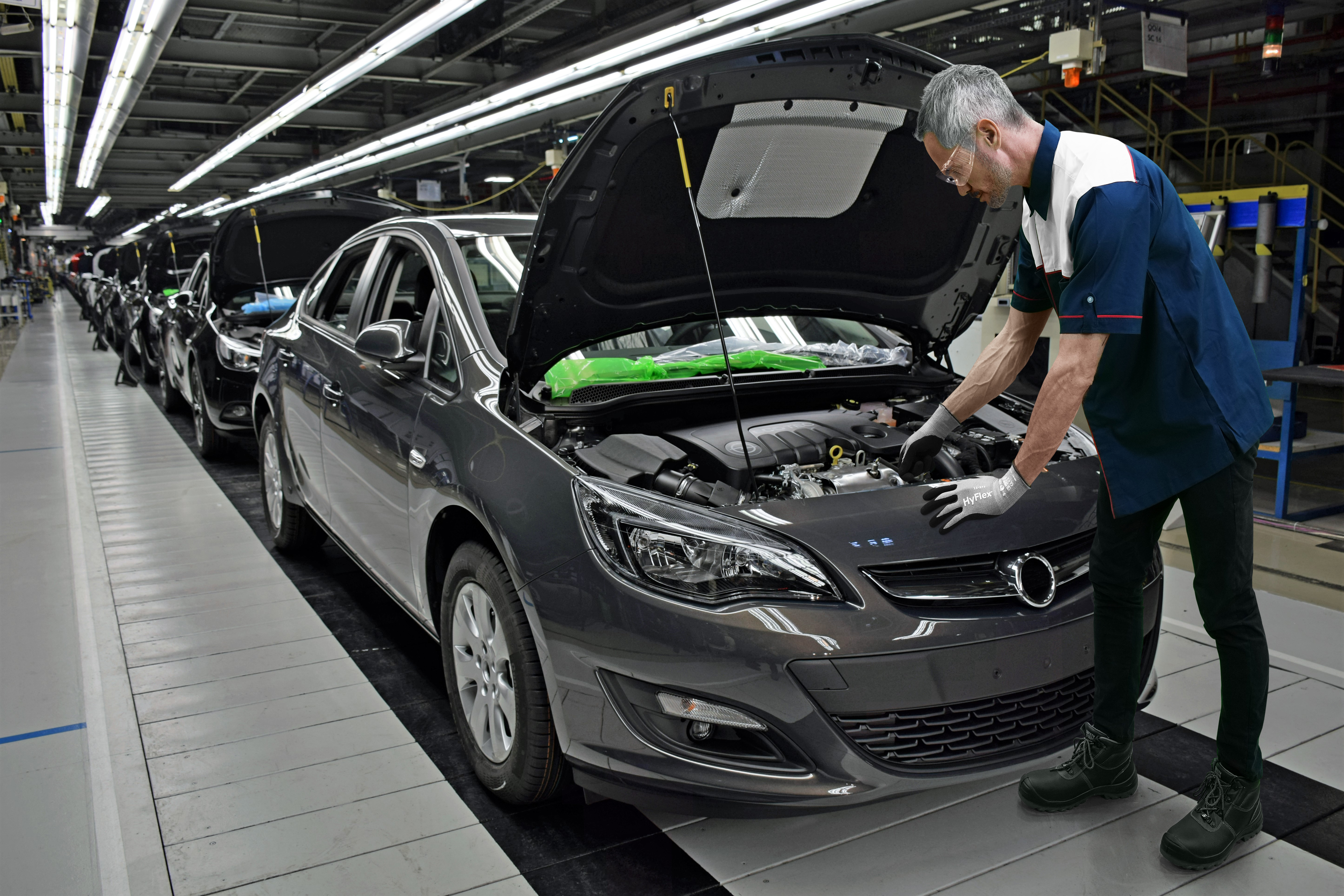 Worker adjusts car engine wearing HyFlex® 11-571 mechanical gloves, ensuring precision and safety in a repair setting.