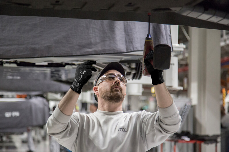 Worker wearing HyFlex® 11-591 mechanical gloves assembles car parts, ensuring safety and precision in the automotive assembly process.