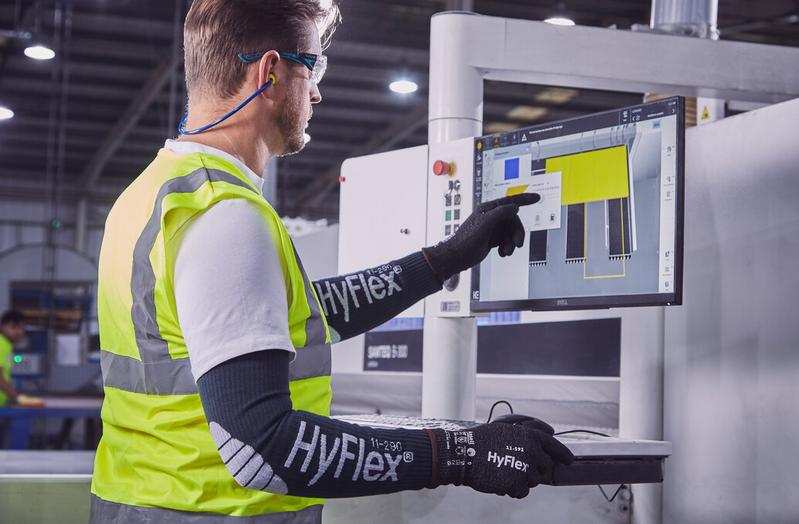 Worker wearing HyFlex® 11-591 mechanical gloves operates a computer to review tool settings, ensuring safety and efficient adjustments.