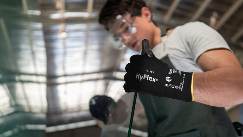 Operator wearing HyFlex® 11-757 mechanical gloves handles a glass sheet, ensuring safe grip and careful positioning during transport.