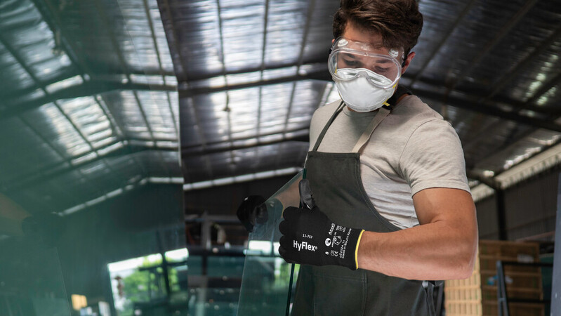 Operator wearing HyFlex® 11-757 mechanical gloves handles a glass sheet, ensuring safe grip and careful positioning during transport.