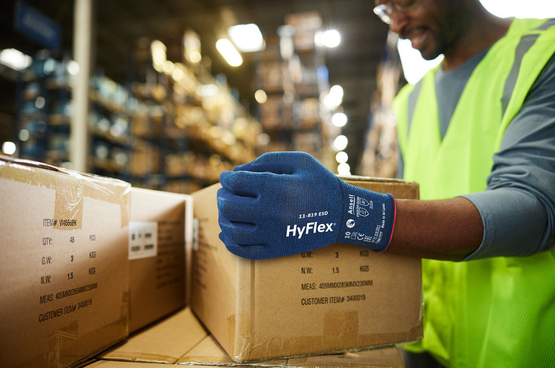 Worker wearing HyFlex® 11-819 ESD mechanical gloves moves boxes in a warehouse, ensuring grip and protection during lifting tasks