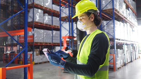 Worker checks orders on a tablet in a warehouse while wearing HyFlex® 11-819 ESD mechanical gloves for safety and precision.
