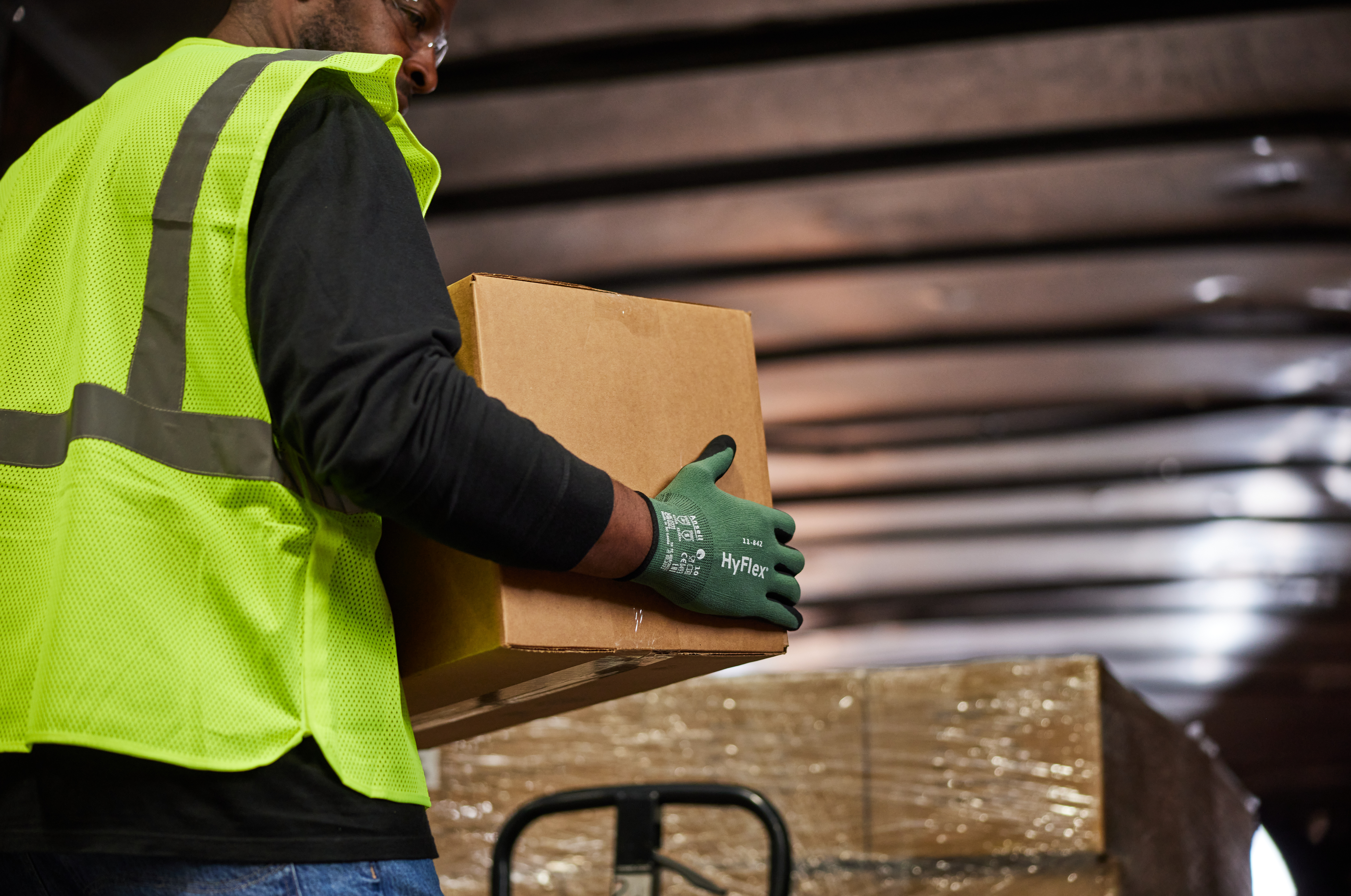 Worker wearing HyFlex® 11-842 mechanical gloves moves boxes in a warehouse, ensuring grip and protection during lifting tasks.