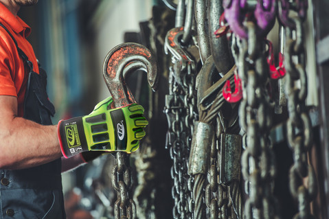 Worker in RINGERS® R267 protective gloves handles a large metal hook among heavy chains, preparing equipment for lifting operations in an industrial setting.